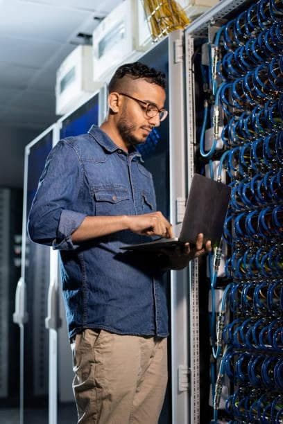 An engineer working on a laptop beside server cabling